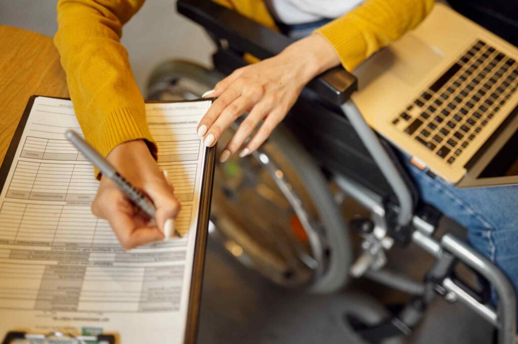 Rollstuhlnutzerin füllt barrierefreies Formular aus, Laptop liegt auf dem Schoß.