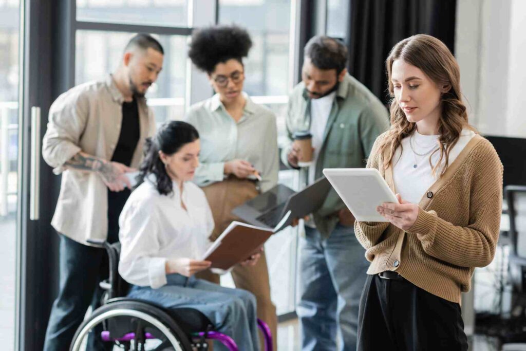 Ein diverses Team arbeitet gemeinsam an Dokumenten und digitalen Geräten; eine Frau im Rollstuhl ist aktiv eingebunden. Die Szene steht exemplarisch für barrierefreie Zusammenarbeit und unterstreicht die Bedeutung von Accessibility-Tests im inklusiven Arbeitsumfeld.