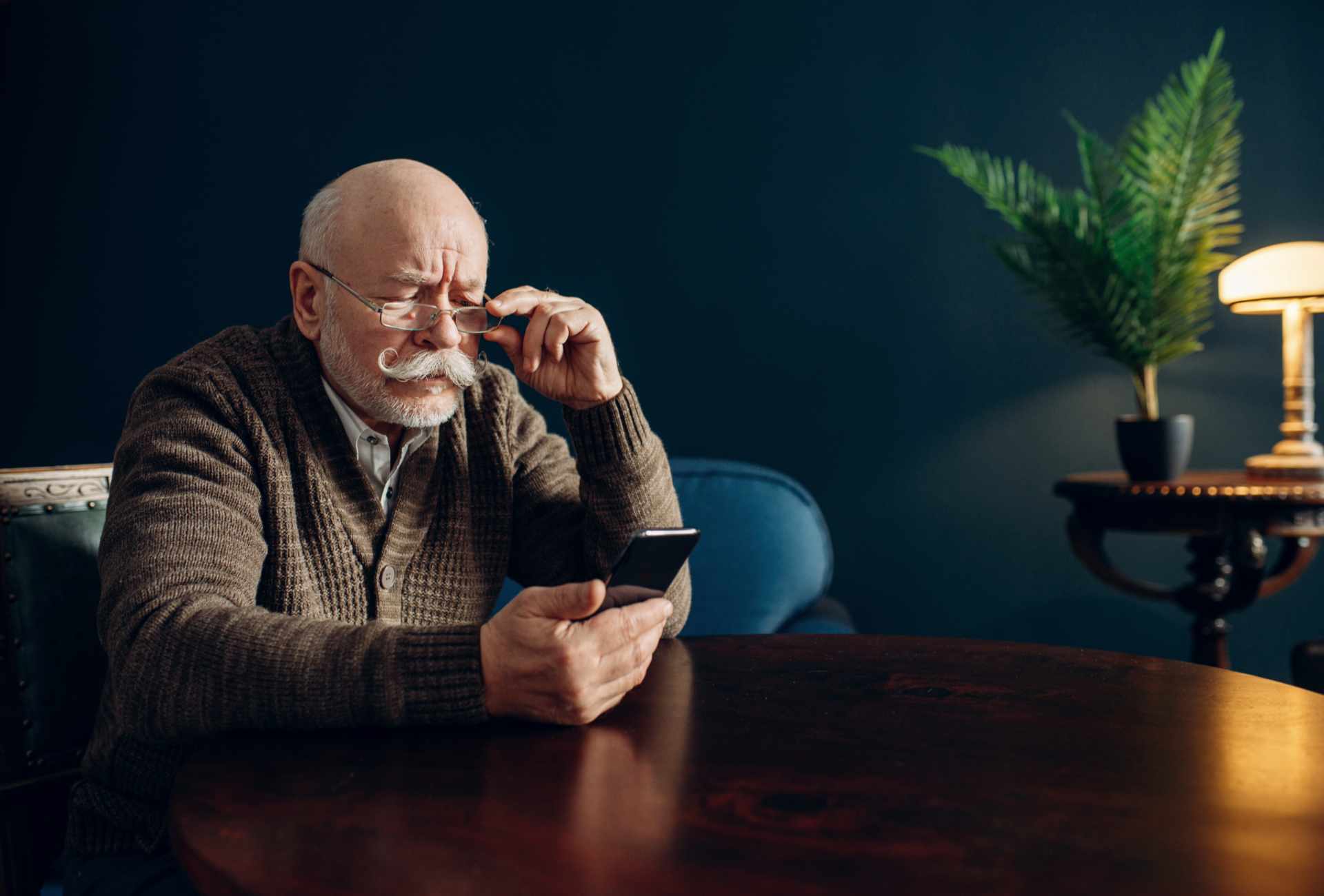 Älterer Mann mit Brille schaut konzentriert auf Smartphone – Herausforderung der digitalen Barrierefreiheit im Alter.